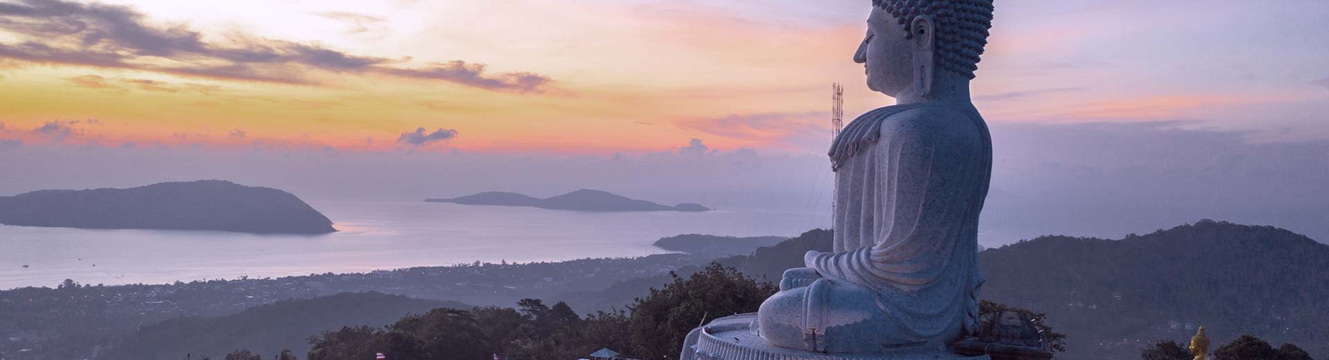 A religious statue sits on top of a hill, overlooking a coastline in the half-light of dusk.