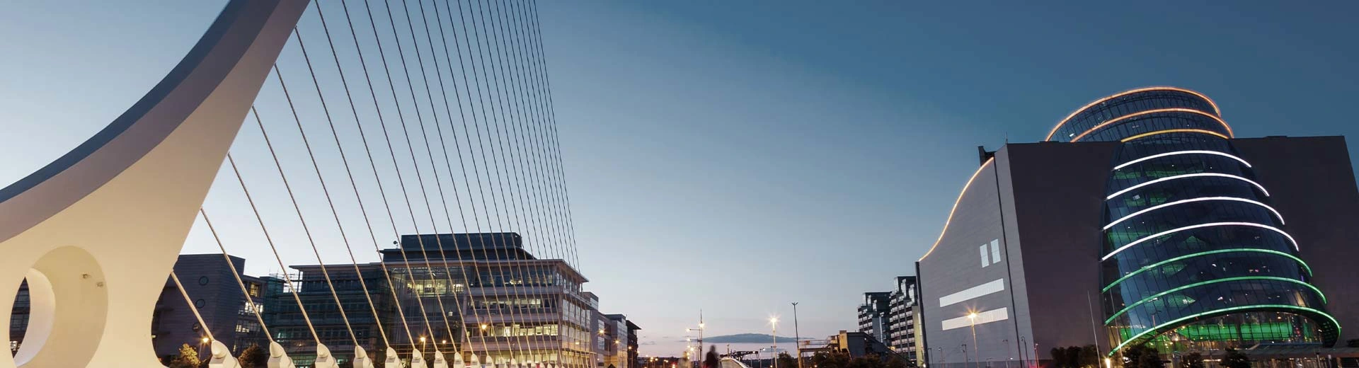 Commercial buildings and a modern bridge during a darker part of the day in Dublin.