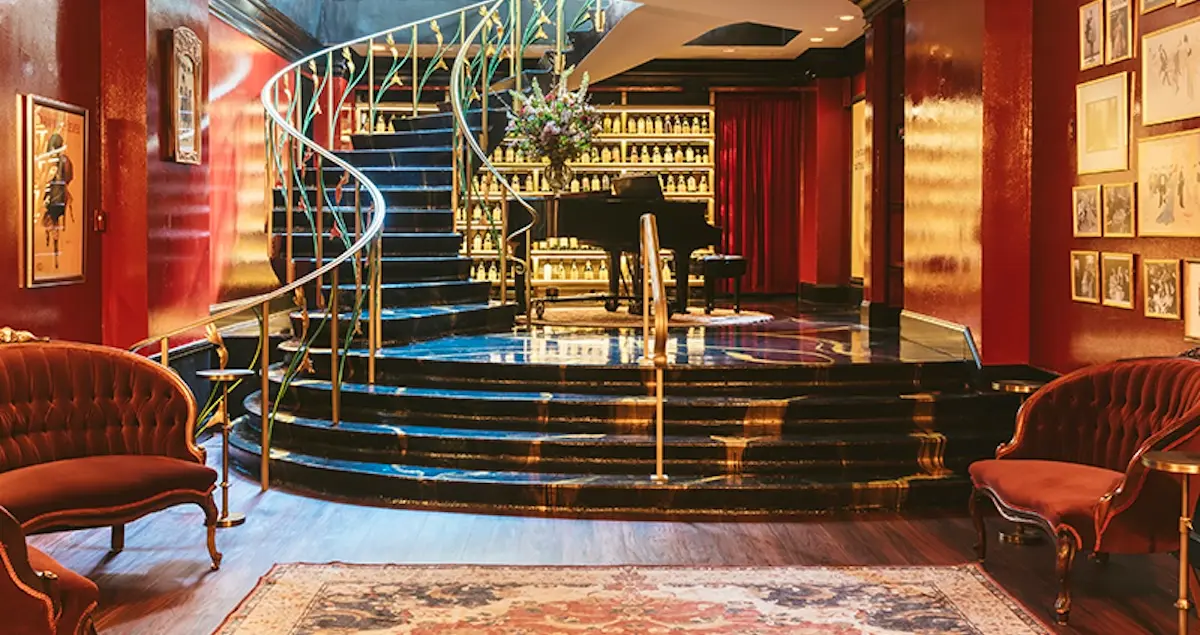 View of the staircase inside the Astor private members club in Chicago, showing a grand piano and seats in the foreground.