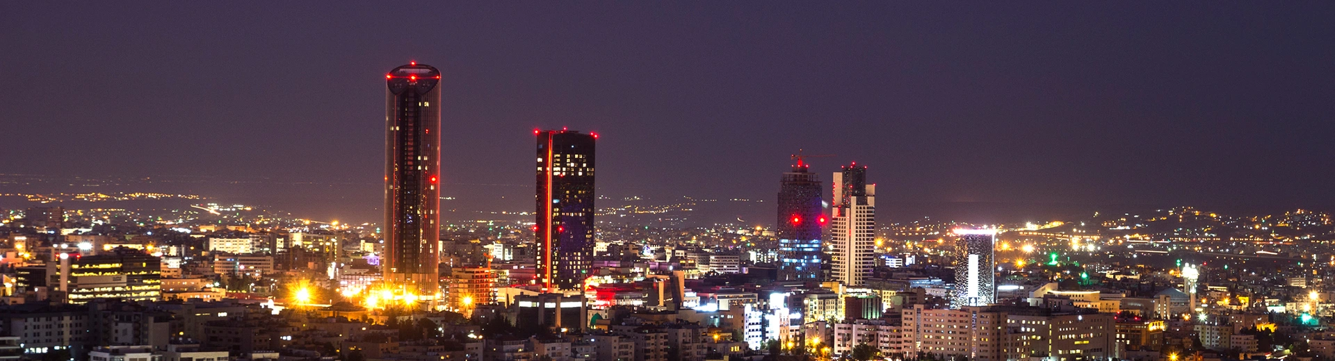 A dark night in Amman as three skyscrapers light up the surrounding area.