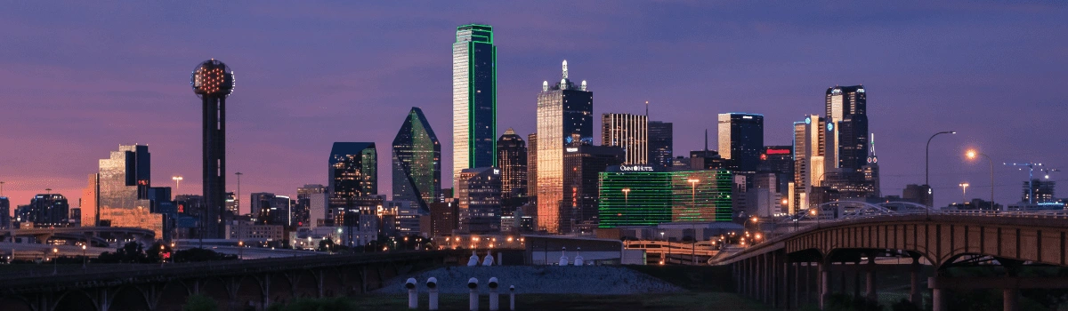 The buildings of the Dallas skyline lit by a purple dusk sky.