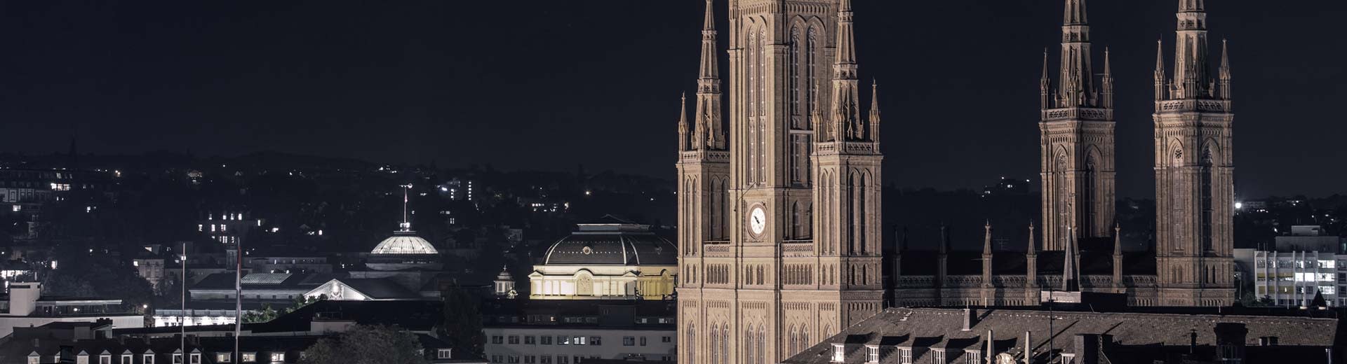 The world-famous Marktkirche dominates the foreground of Wiesbaden, with the lights of buildings in the distance.