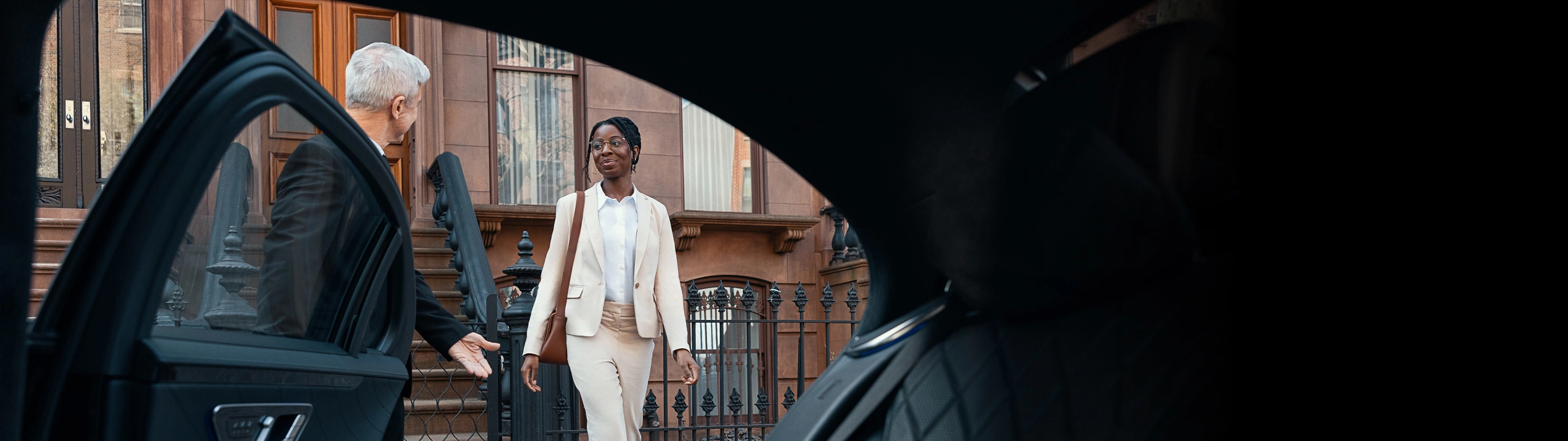 Chauffeur opens the door for a business woman in front of a brownstone apartment.