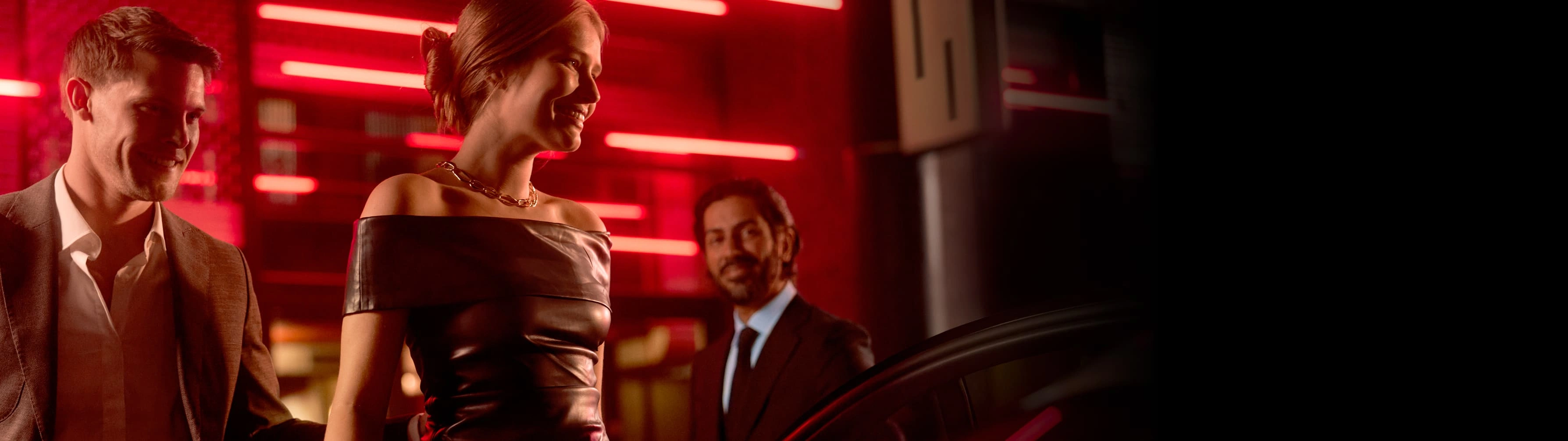 A stylish couple get into a Blacklane limousine service as their suited chauffeur holds the door open for them.