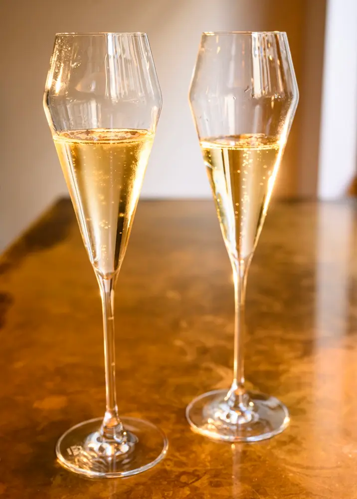 Two elegant flutes of Champagne sitting on an oak counter.