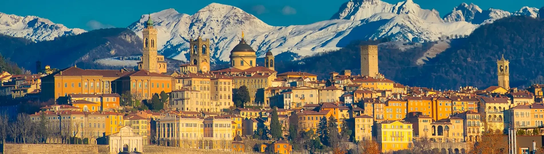 A shot of the hilltop city of Bergamo in the winter sun, with snowy mountains in the background.