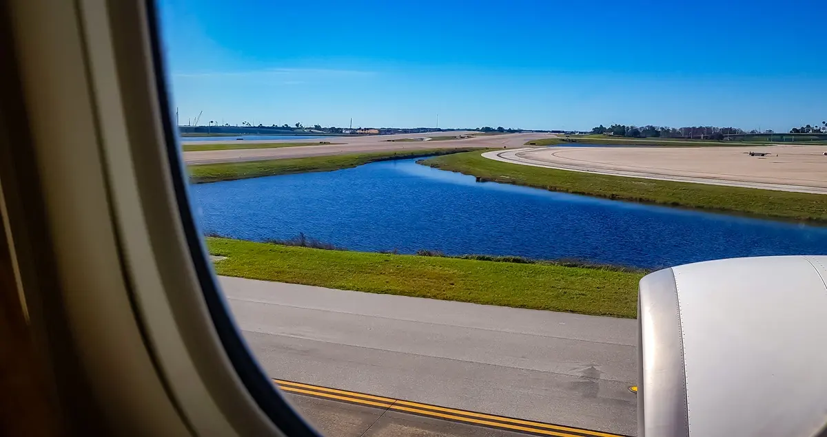 Shot of the main runway of Orlando MCO Airport through the window of an airplane, with the engine and a water pond in the centerground.
