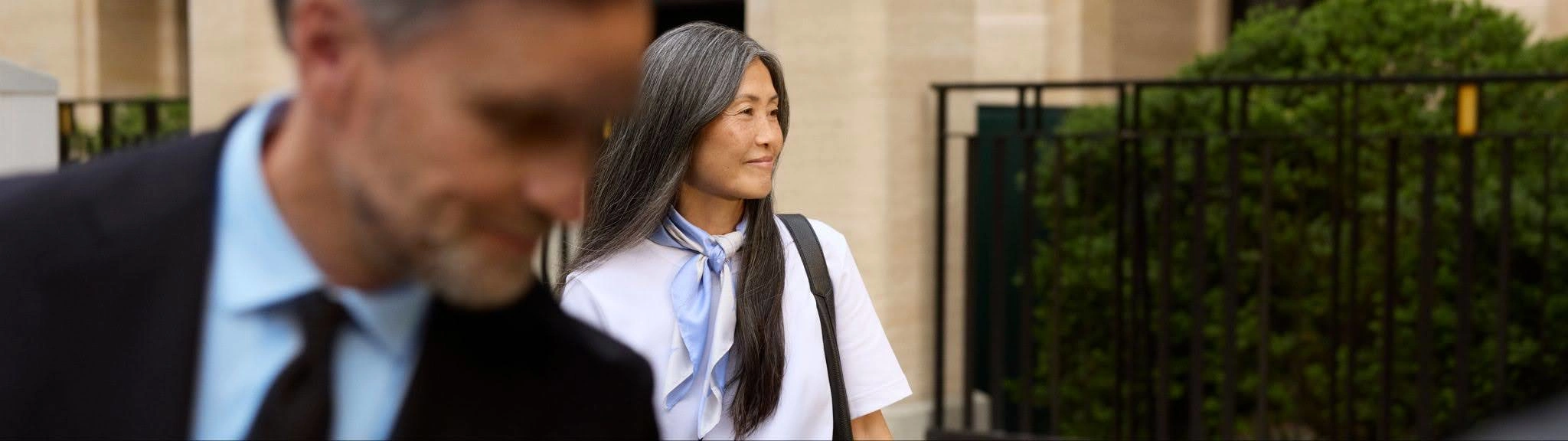 A woman smiles in the background as a chauffeur in the foreground works at her car.