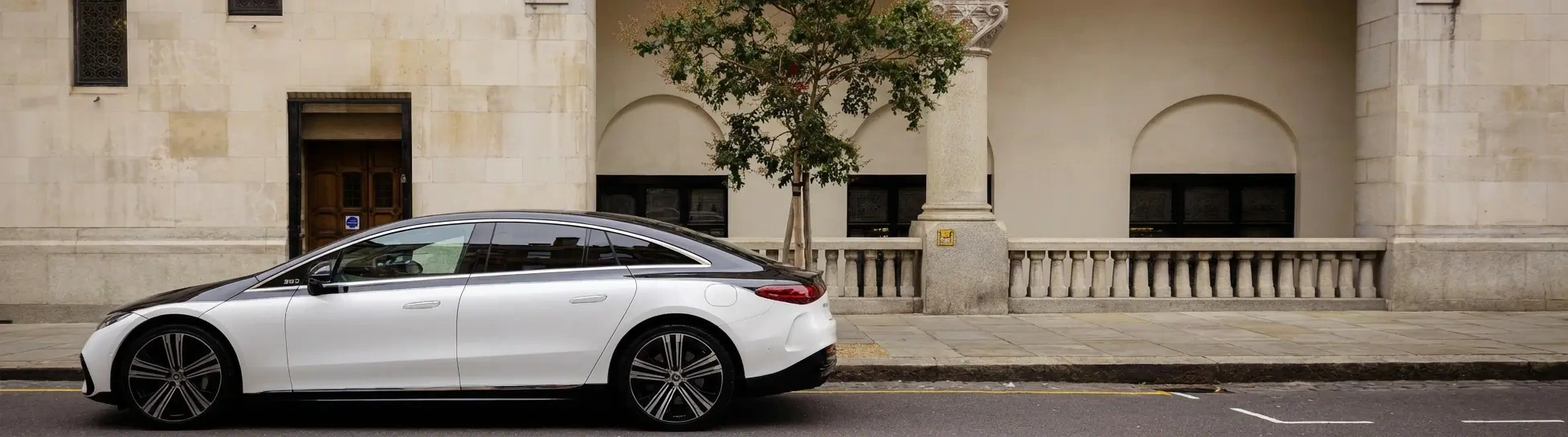 A two-tone Mercedes EQS serving as a Blacklane limo is parked outside an elegant building on a city street.
