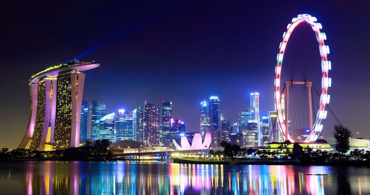 The Marina Bay area of Singapore lit up at night for the Singapore grand prix, with the Marina Bay Sands hotel on the left and a big wheel on the right.