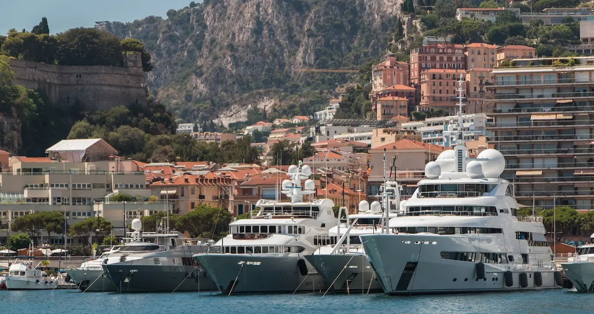 Shot of superyachts sitting in Monaco's Port Hercule, with buildings and an old fort rising in the background.