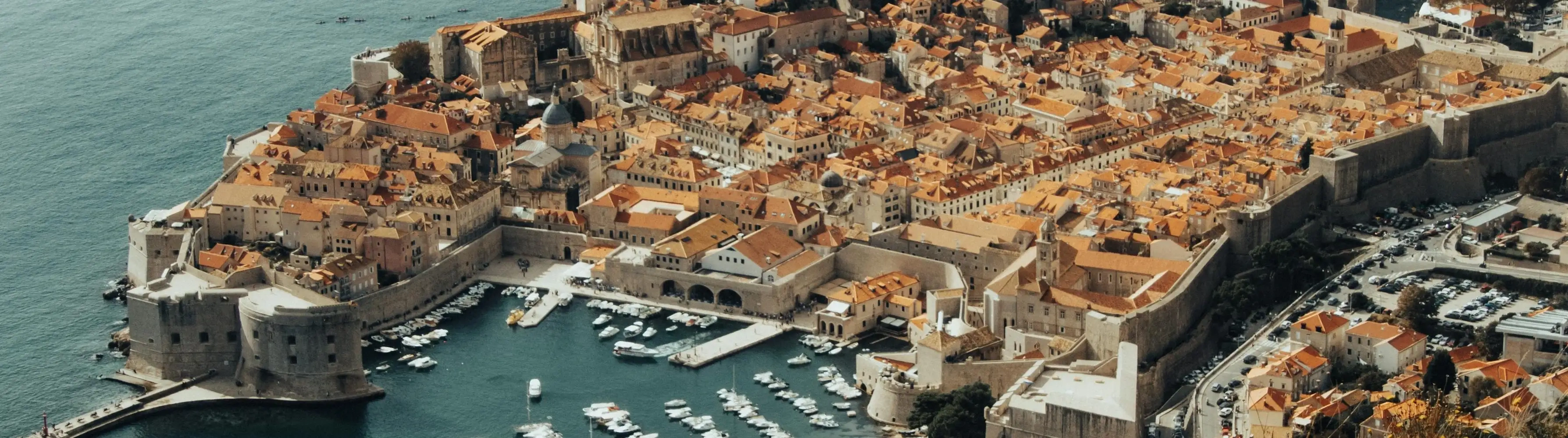 Shot of Dubrovnik Old Town and its port area from above, showing the old city walls and the orange roofs.