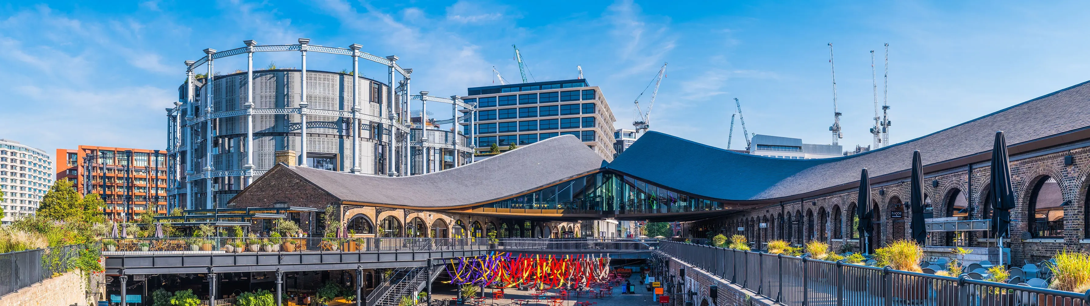 Colourful shot of the exterior area of King's Cross Station with the old gasometer in the background.