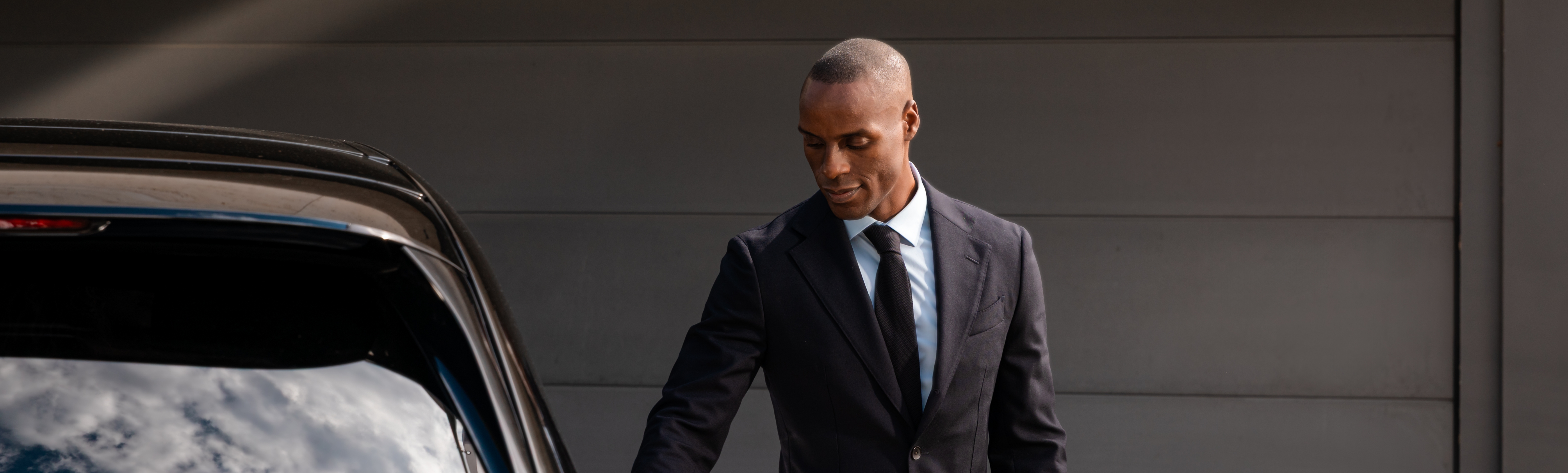 A chauffeur in a suit standing outside a black vehicle.