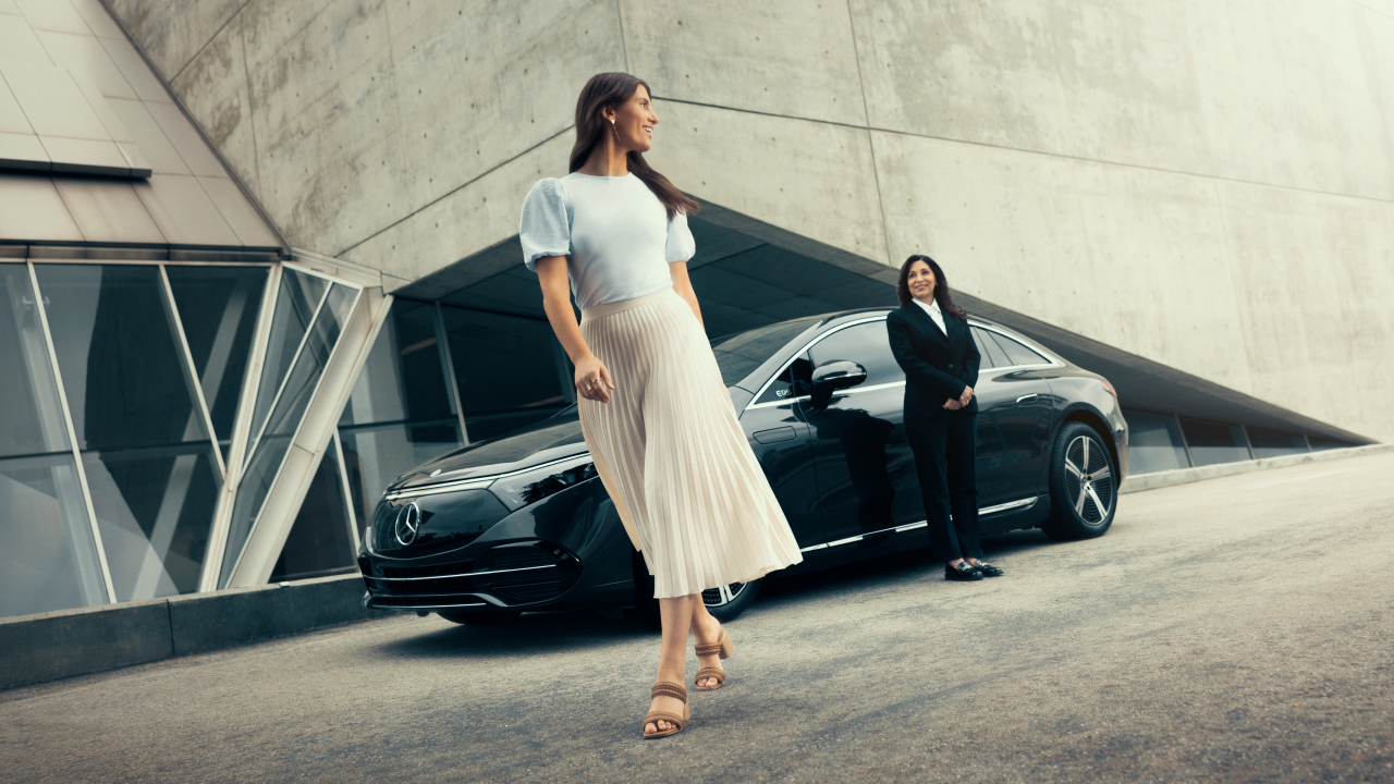 A Blacklane guest departing from a ride looks back at her chauffeur, who stands next to a Mercedes-Benz.