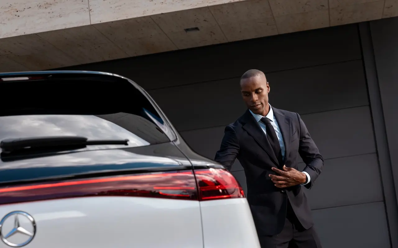 A Blacklane chauffeur about to open the rear door of a two-tone Mercedes SUV.