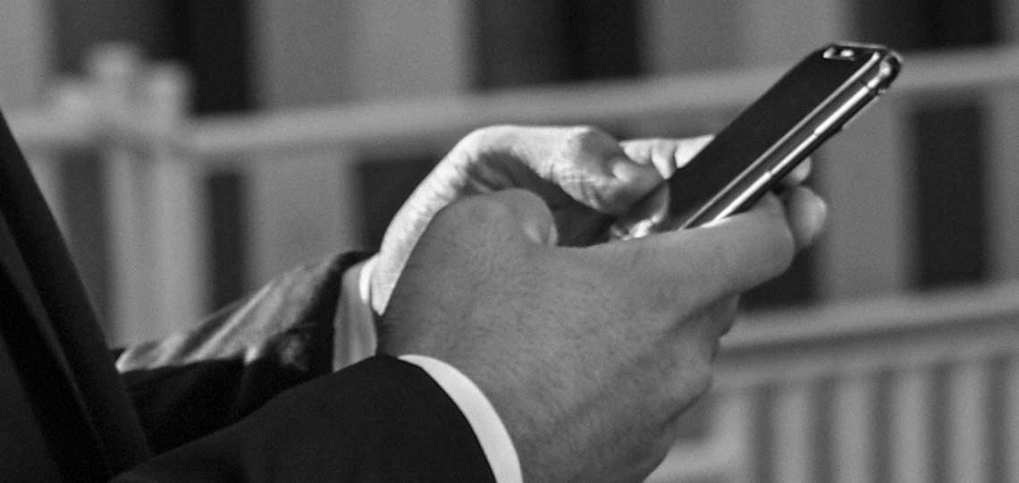 Un hombre con un buen traje sujeta un móvil con ambas manos, mientras usa la app para reservar un traslado.