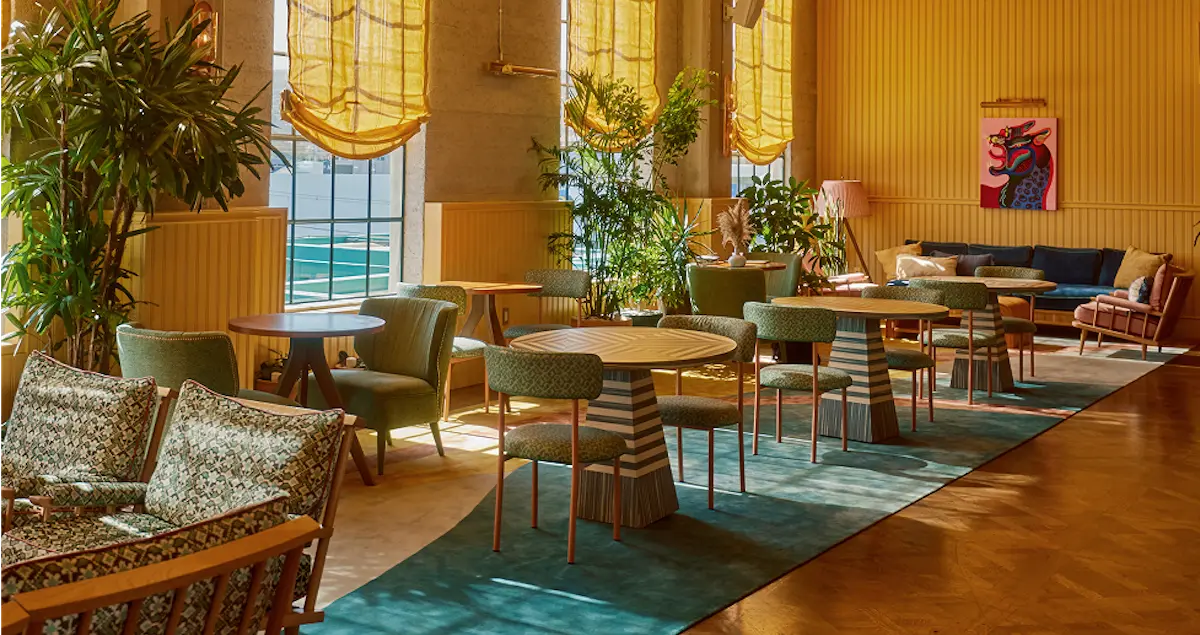 Shot of the sunlit lounge at Heimat private member's club in LA, showing tables, chairs, and wall art.