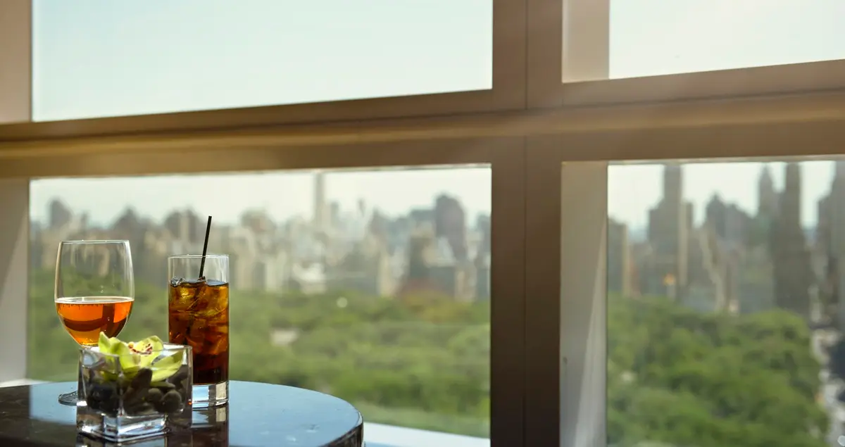 A shot of two drinks in an NYC private members club, with Manhattan skyscrapers and Central Park visible through the window behind.