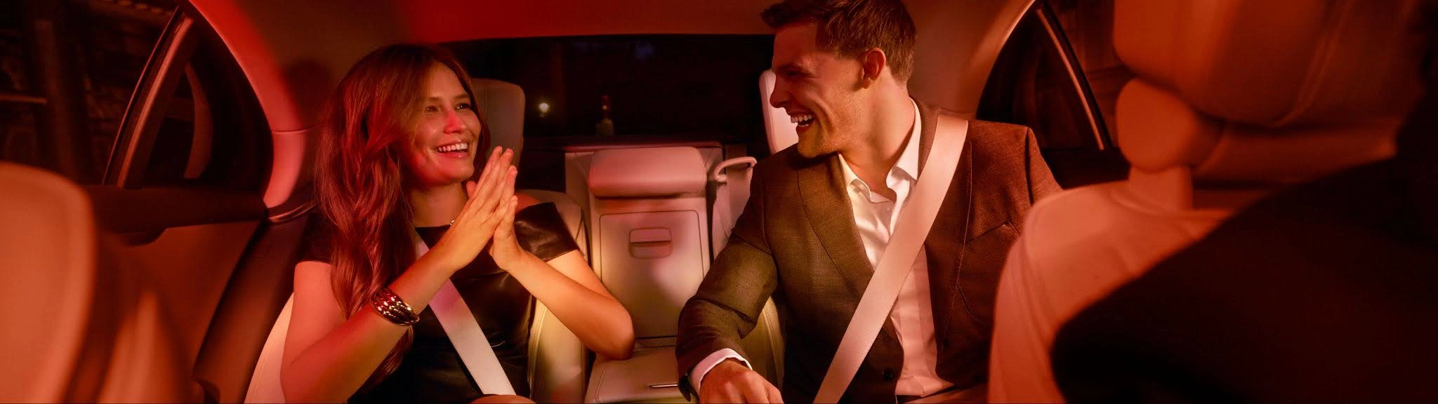 A stylish couple laugh in the backseat of a Blacklane limousine service.