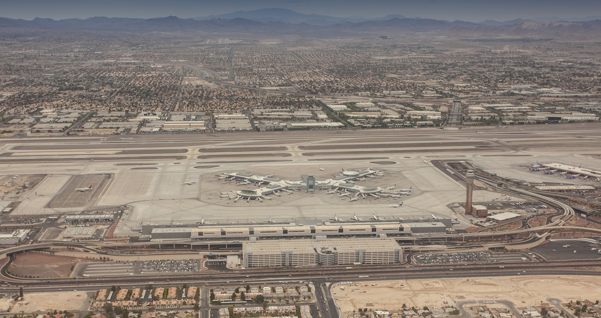 Aerial shot of Las Vegas Harry Reid Airport, showing the main terminal building, the car parking and access roads, runways, and surrounding area.