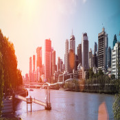 El sol se refleja en el río Brisbane y en la orilla hay árboles y rascacielos.