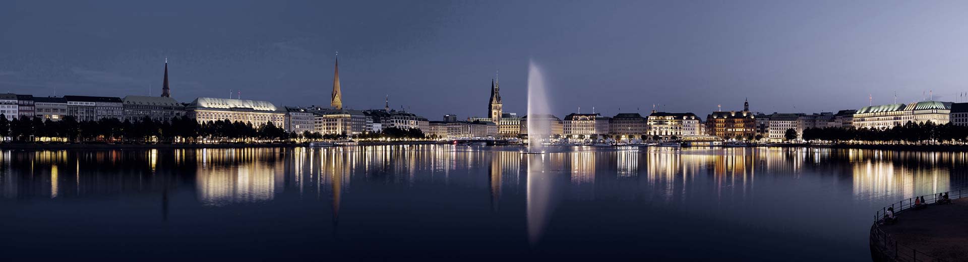 The harbour of Hamburg lit up at night agaisnt a dark blue sky.