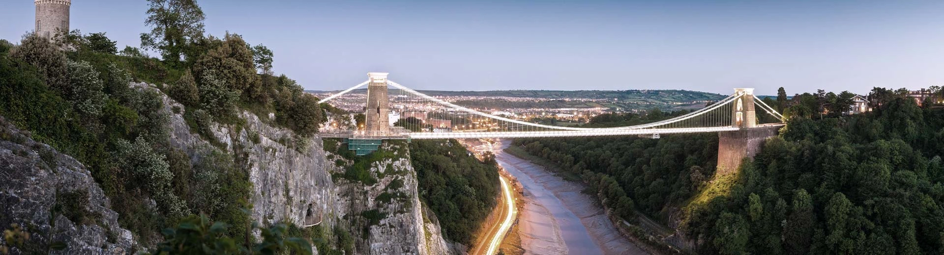 Arbustos verdes en un acantilado de roca a la izquierda con una vista del puente colgante de Clifton en Bristol al centro a la derecha.