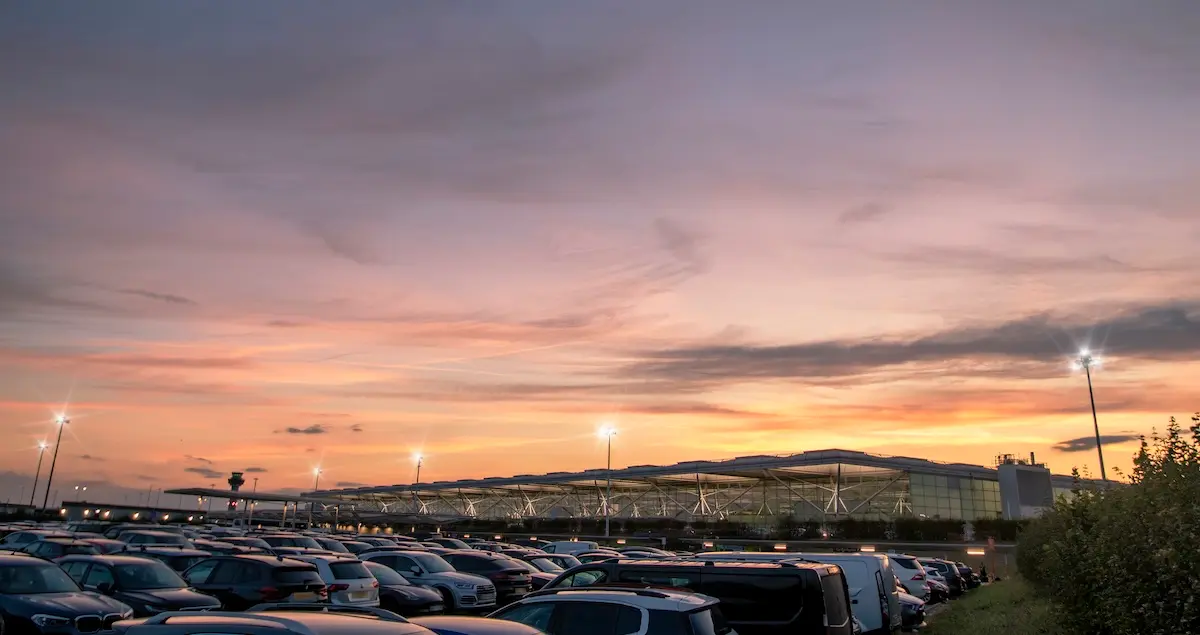 The carpark of Stansted Airport with the terminal in the background at dawn with a sunrise in the background.