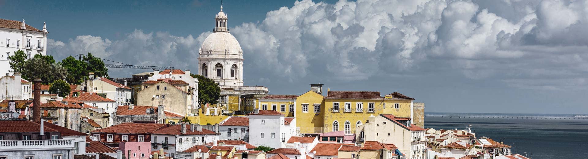 The pastel colored buildigns of Lisbon set against a cloudy sky.