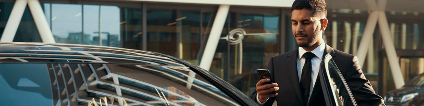 Chauffeur checking cellphone as he gets into his vehicle.