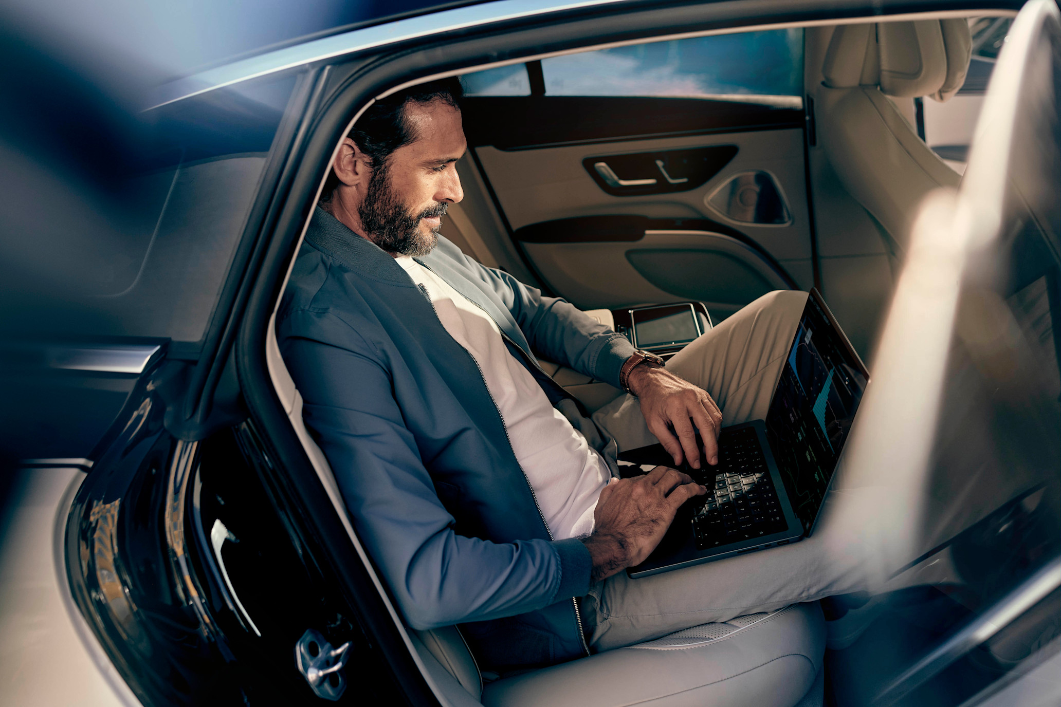 A businessman sits in the back seat of a Blacklane limousine, working on his laptop.
