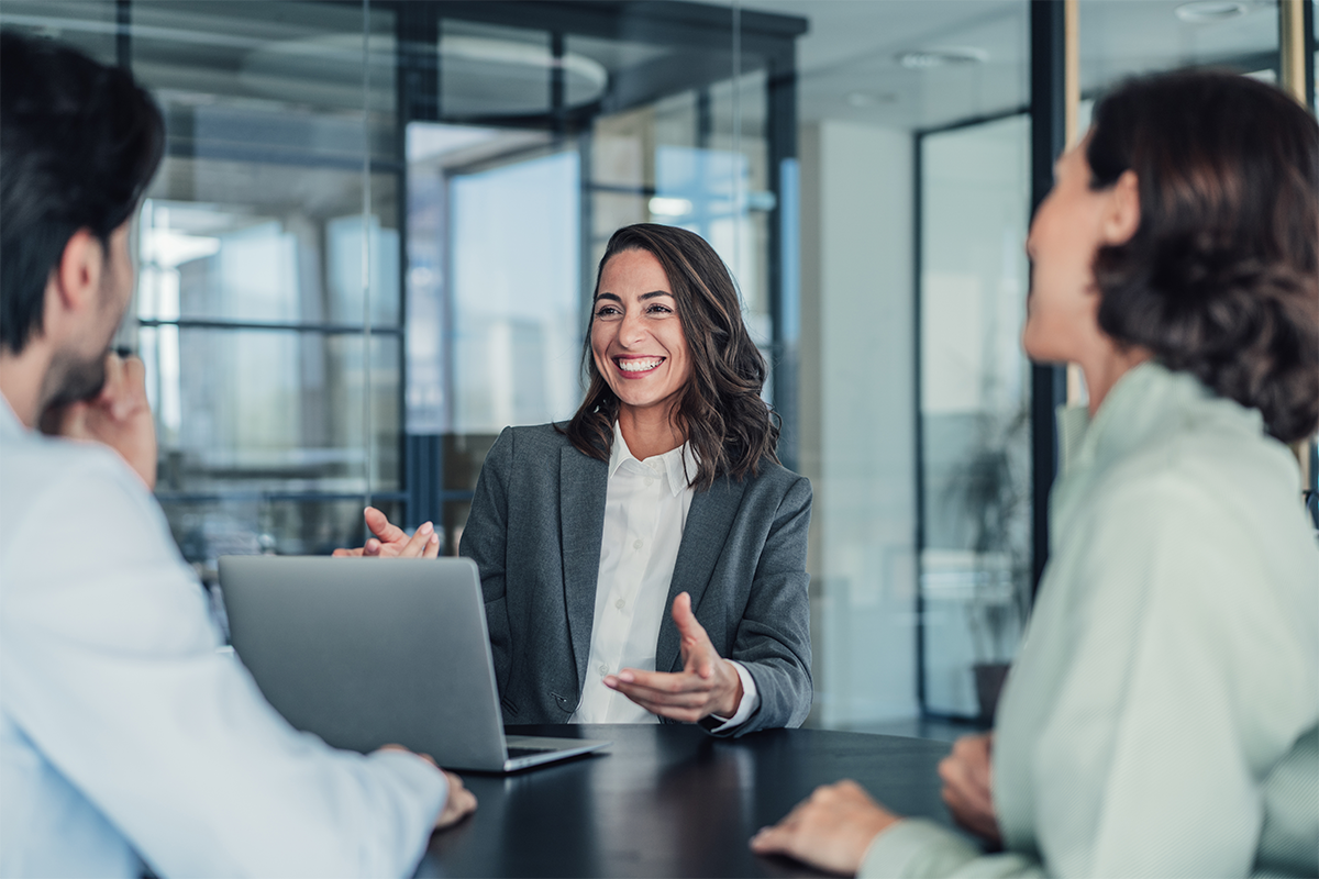 A woman in a suit with a laptop is explaining something to two colleagues.