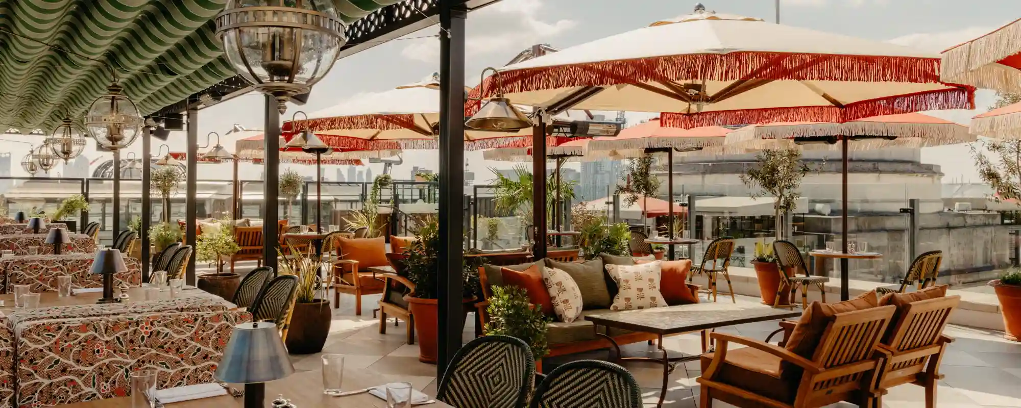 The rooftop bar part of Ned's Club private club in London, with parasols and the skyline in the background.