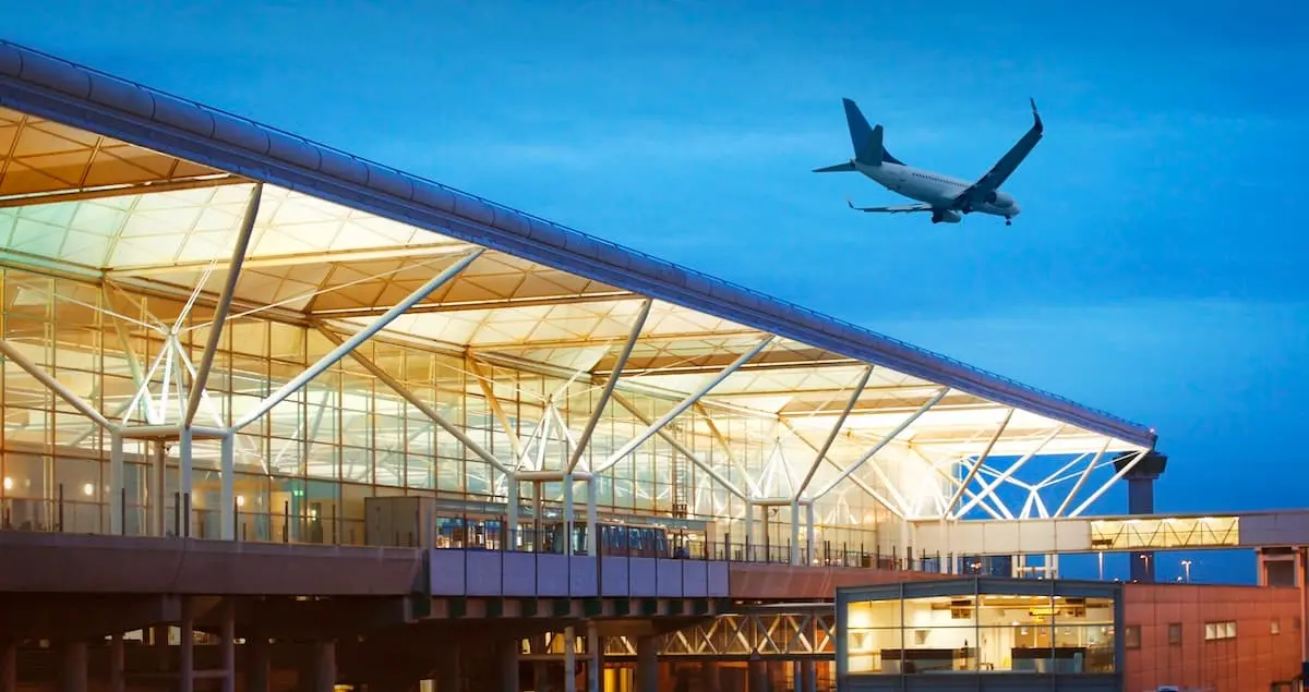 Exterior shot of London Stansted airport by twilight, with a plane landing just above the terminal.