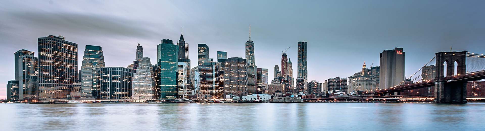 Manhattan skyline lights up the sky at dusk or dawn.