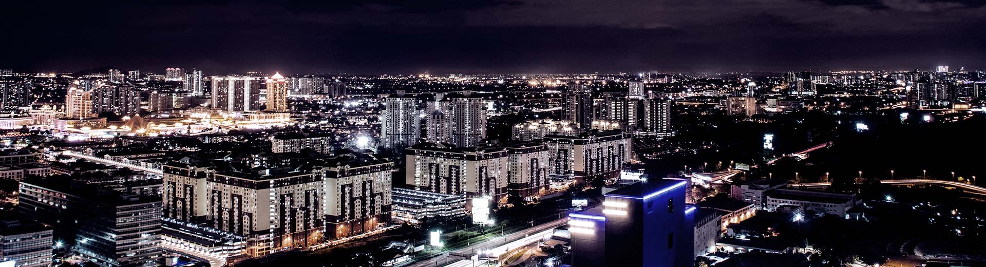 The high-rise buildings of Petaling Jaya illuminate the dark and starless sky above them.
