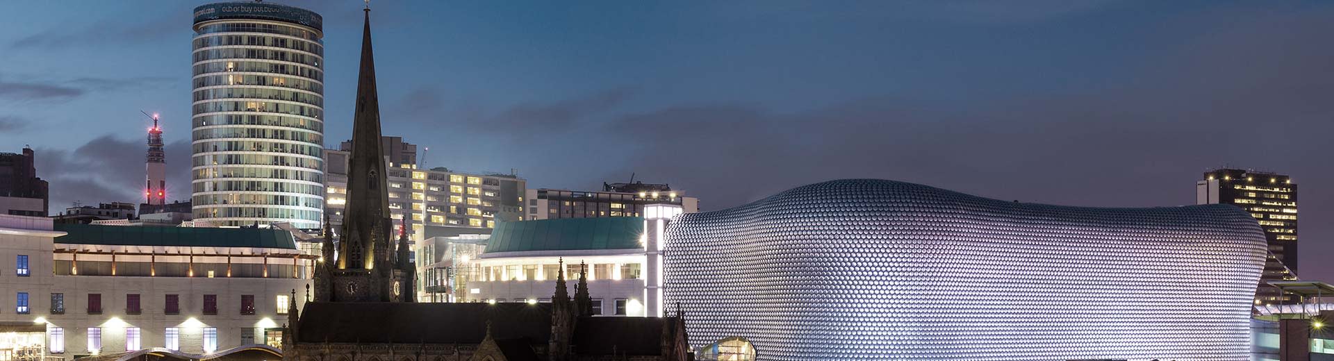 Birmingham during the evening with the Bull Ring on the right and a church on the left.