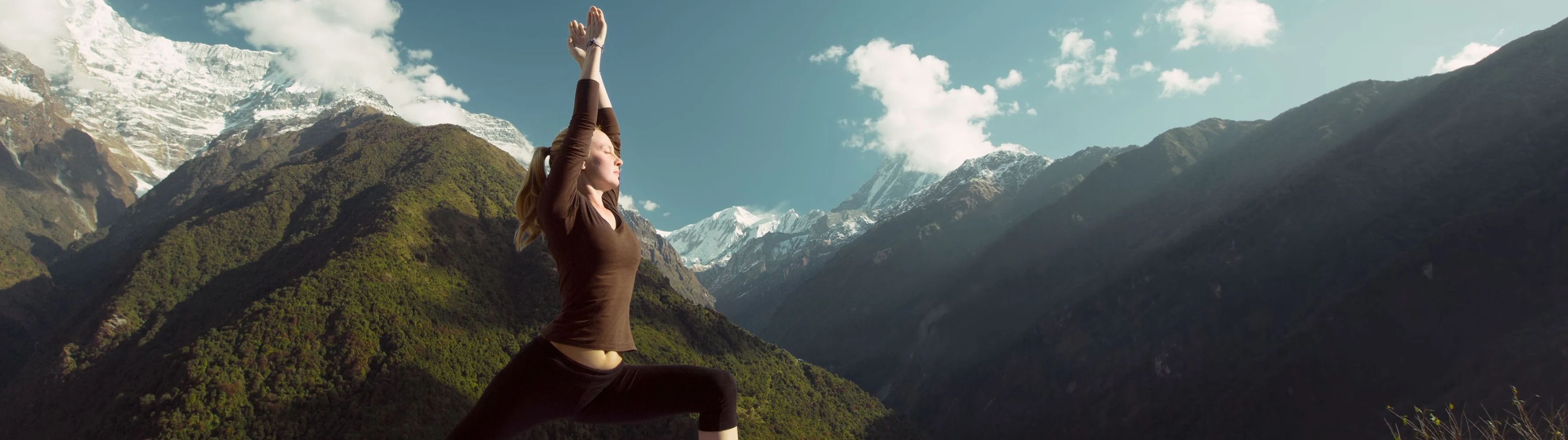 A woman on a luxury travel holiday performs a yoga pose on a mat with snowy peaks in the background.