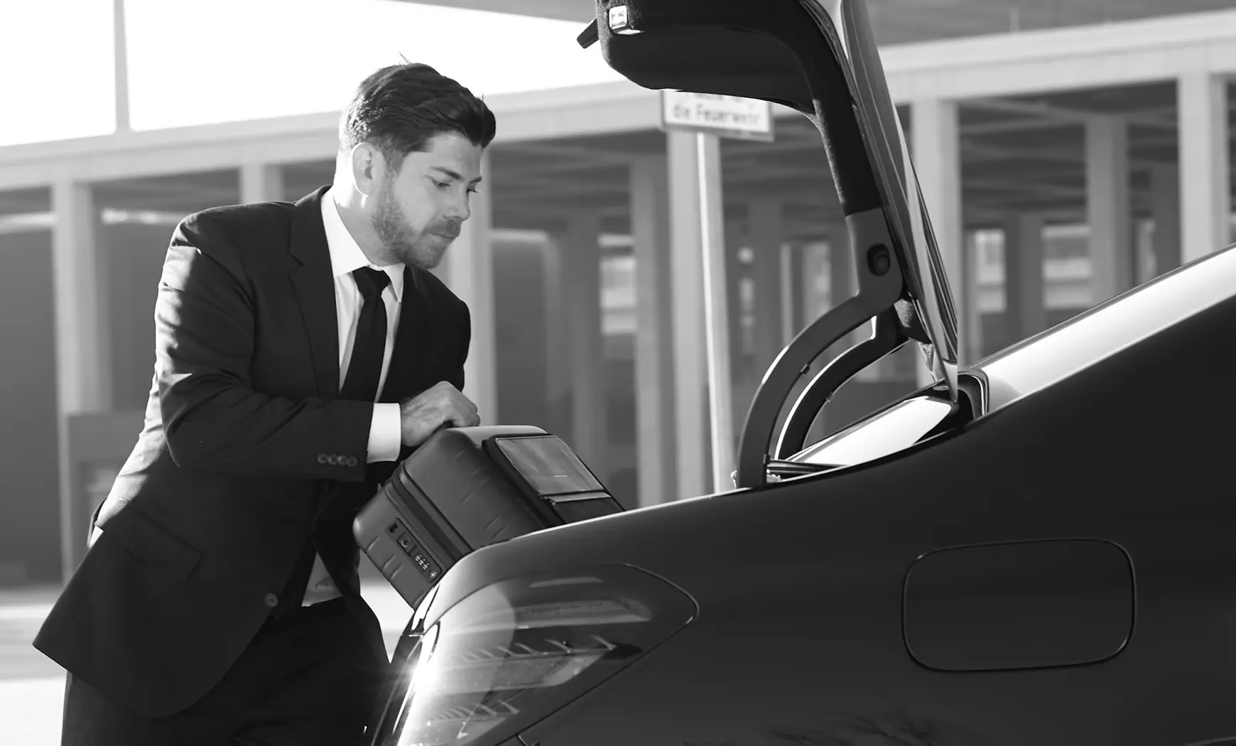 A Blacklane chauffeur stores a passenger's luggage in the trunk of a Mercedes limo.