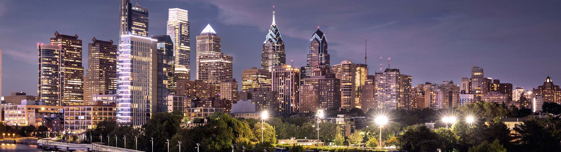 The high-rising Philadelphia skyline at night illuminates the dark sky above.