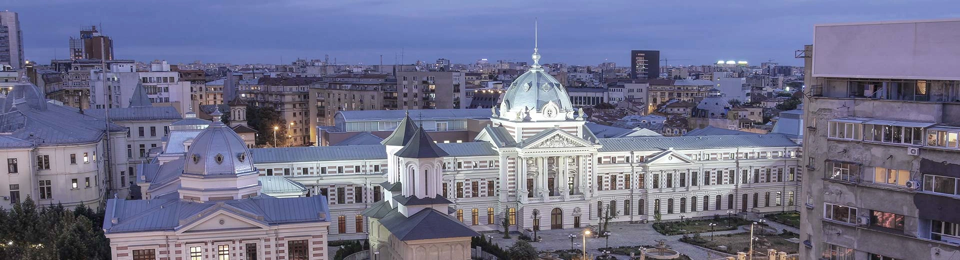 Vista de ojos de pájaros de la ciudad de Bucarest, con el hospital Coltea en foco. Cielo azul de la tarde y luces de la ciudad.