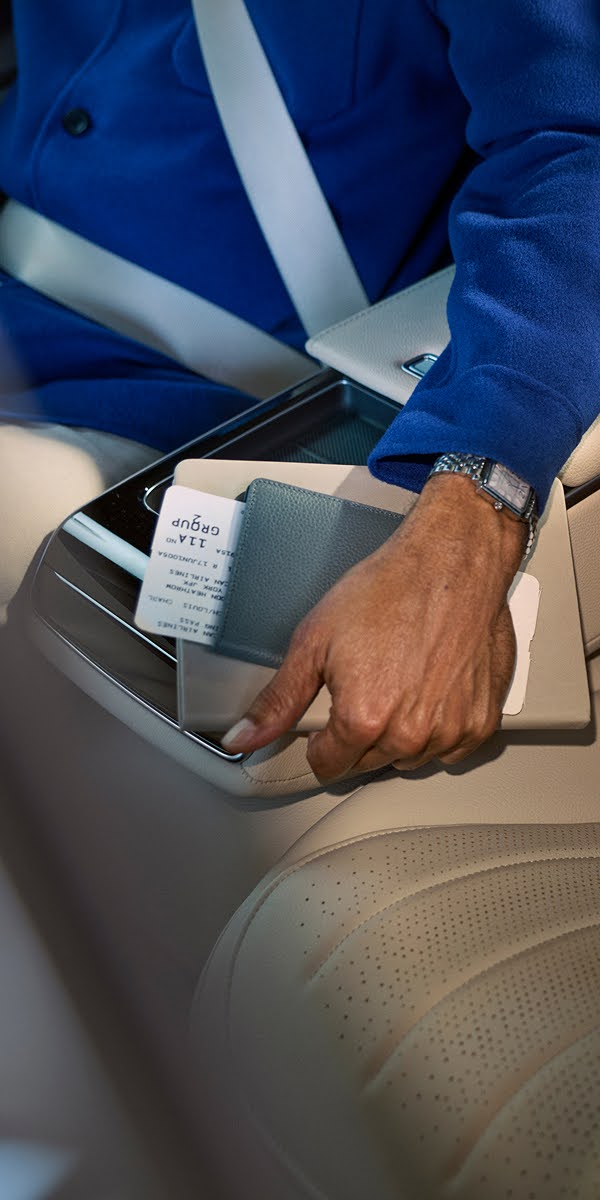 A man's hand in the backseat of a car holding a passport and an airline ticket.