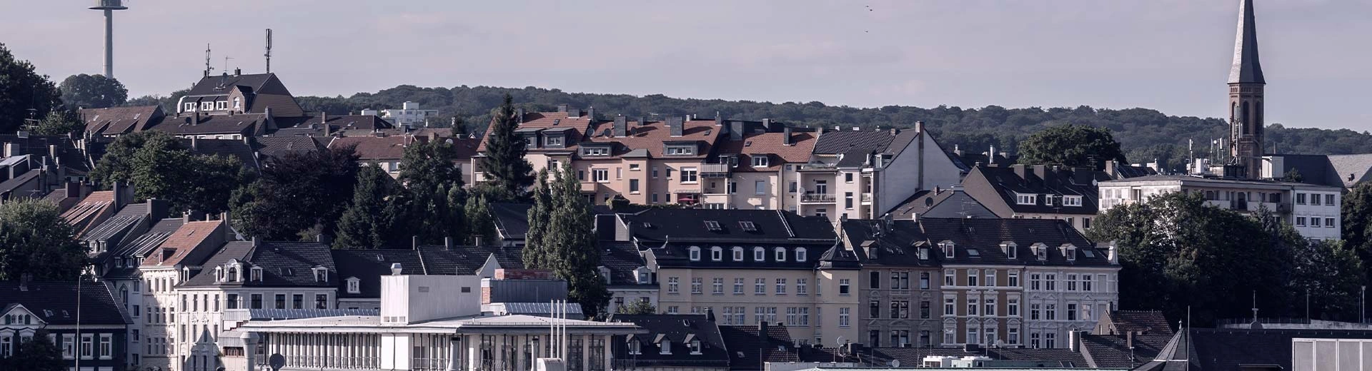 Un mélange de bâtiments résidentiels typiques de Wuppertal au premier plan est contrasté par des collines vertes au loin.