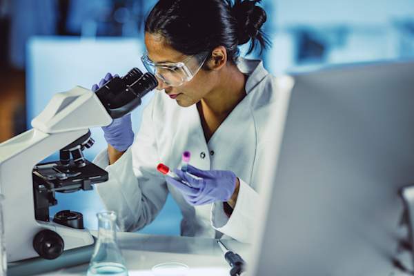 Scientist Looking Through a Microscope holding blood tubes