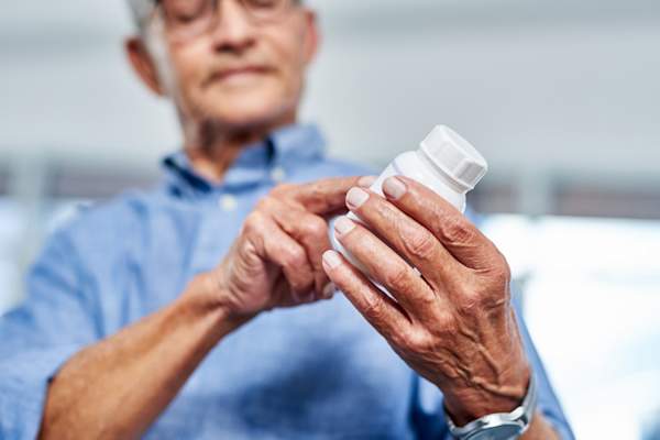 elderly man reading the contents on a bottle of medication