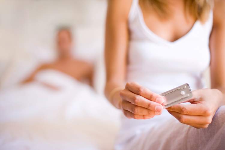 Woman taking the morning-after pill in bed, her partner is behind her