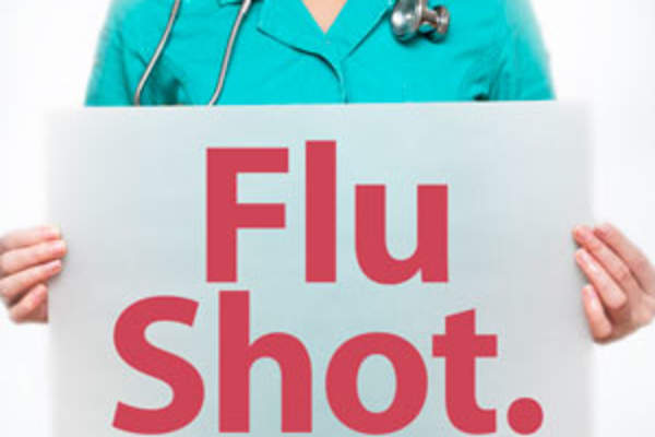 A clinician holding a Flu Shot sign