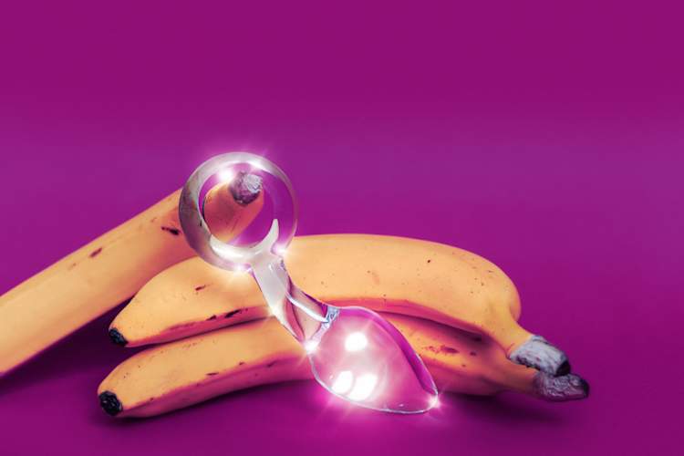 Glass anal sex toy and a yellow banana on a colored background