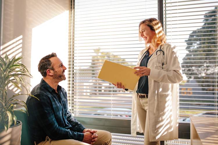 Smiling female doctor holding a medical report file and talking with male patient sitting on sofa